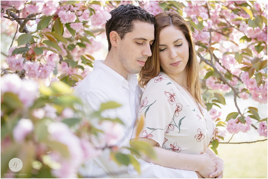 couple cuddling by cherry blossom tree at spring lake engagement session in new jersey 
