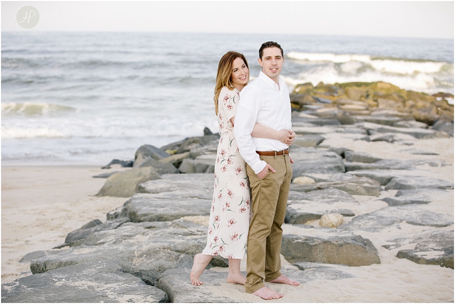 couple on rocks on beach at spring lake engagement session in new jersey 