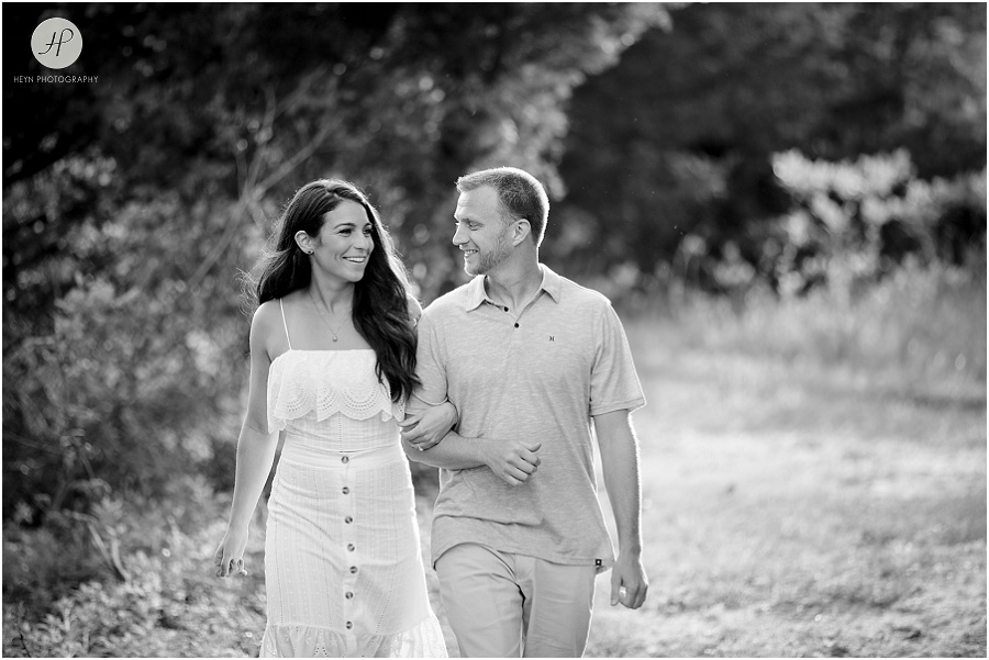 black and white of engaged couple walking in field during sunset in manasquan beach engagement shoot