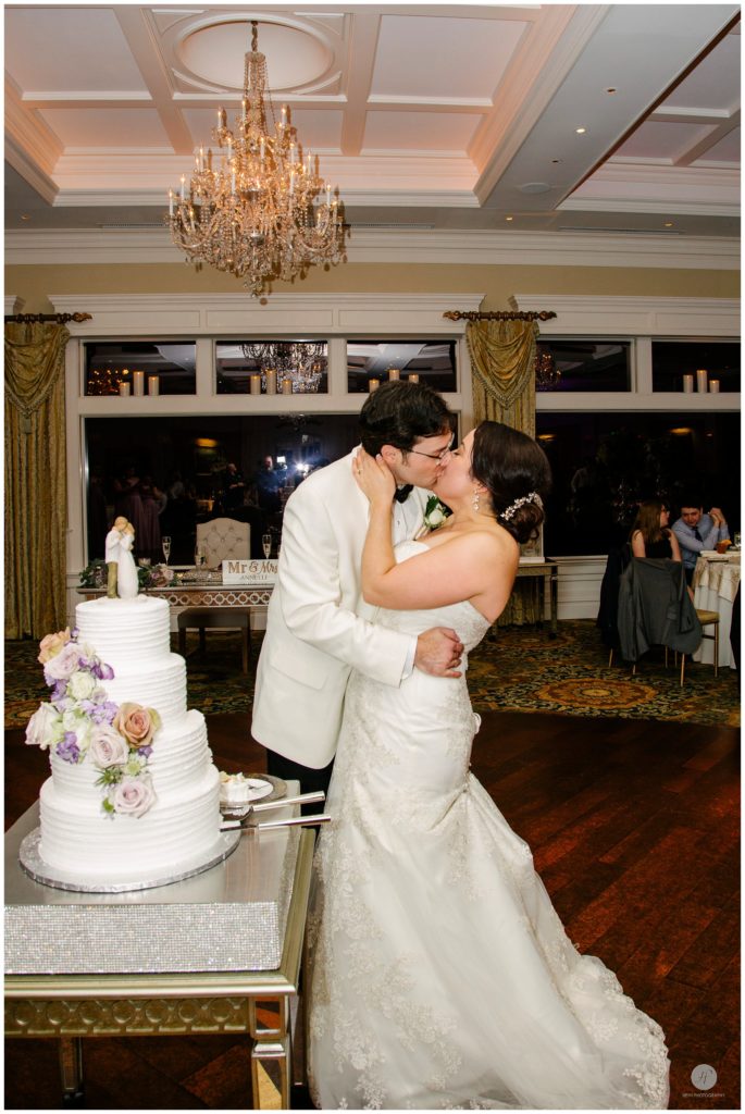 bride and groom kiss when cutting wedding cake